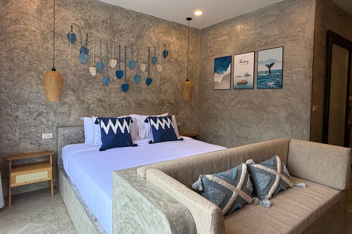 A bedroom with a bed, a sofa, a wall with a textured finish, and hanging decorations.