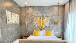 Une chambre moderne avec un grand lit, des œuvres d’art décoratives au mur, des décorations murales en macramé et un coin salon confortable.