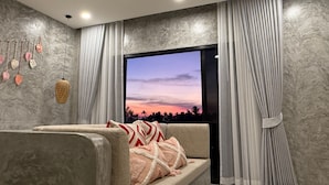 Une chambre moderne dotée d’une grande fenêtre, d’un canapé agrémenté de coussins à motifs et d’un luminaire fixé au mur.