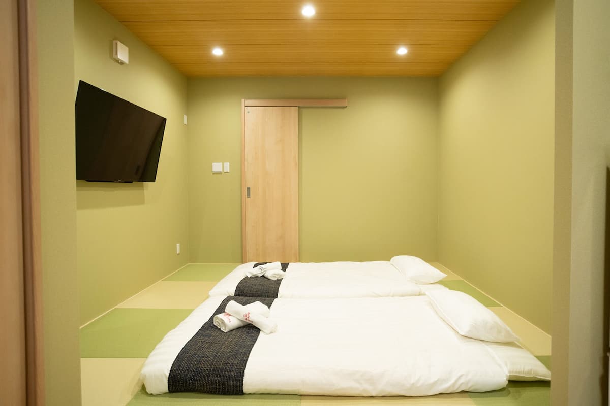 A room with a bed, a flat-screen TV mounted on the wall, and a wooden door.