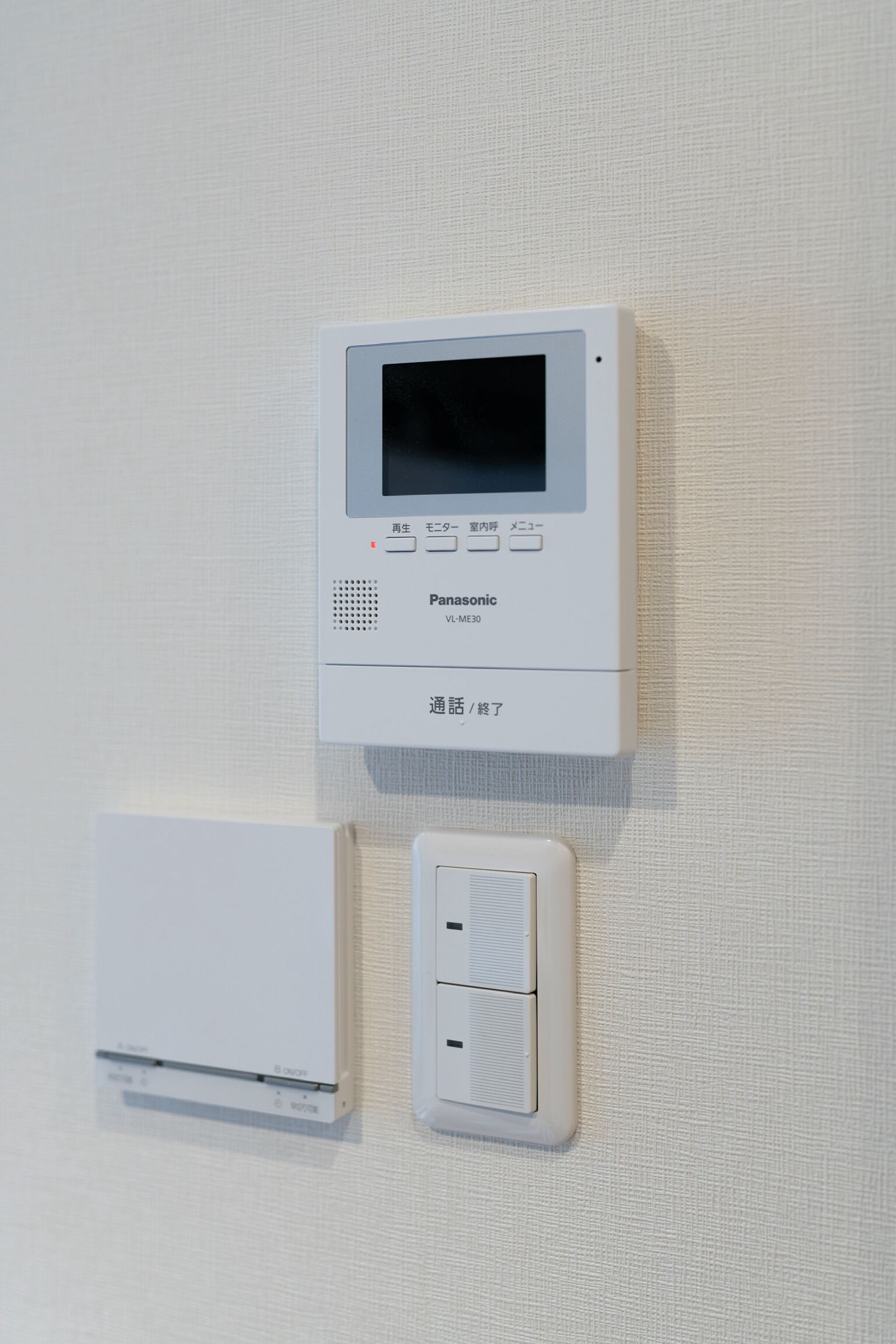 A Panasonic thermostat and a wall-mounted control panel on a textured wall.