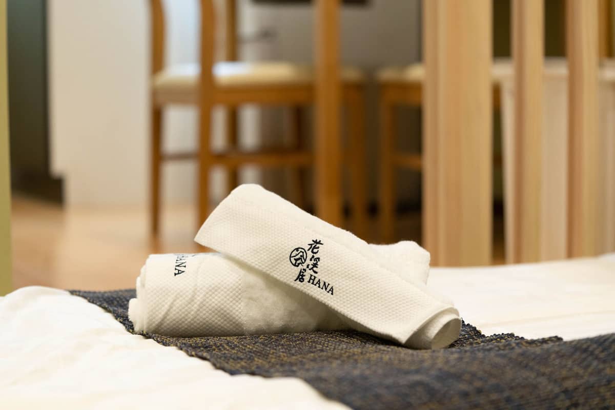 A neatly made bed with a white towel and a folded towel with Japanese characters on it.