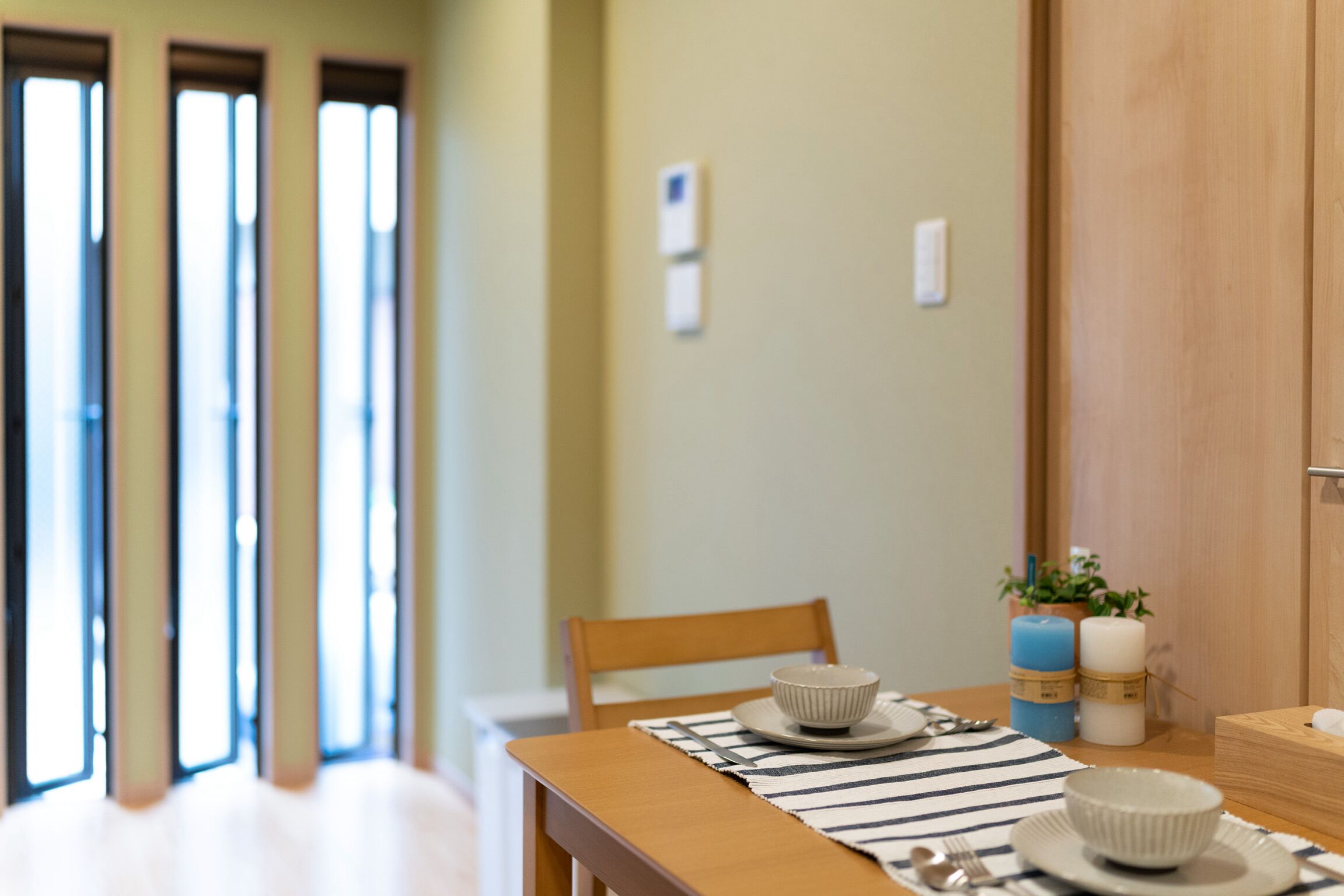 Un comedor con una mesa de madera, un mantel individual a rayas y dos boles. Hay velas y una planta pequeña sobre la mesa.