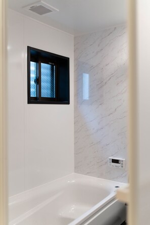Une salle de bain moderne avec une baignoire blanche, une petite fenêtre à cadre noir et un mur en marbre.