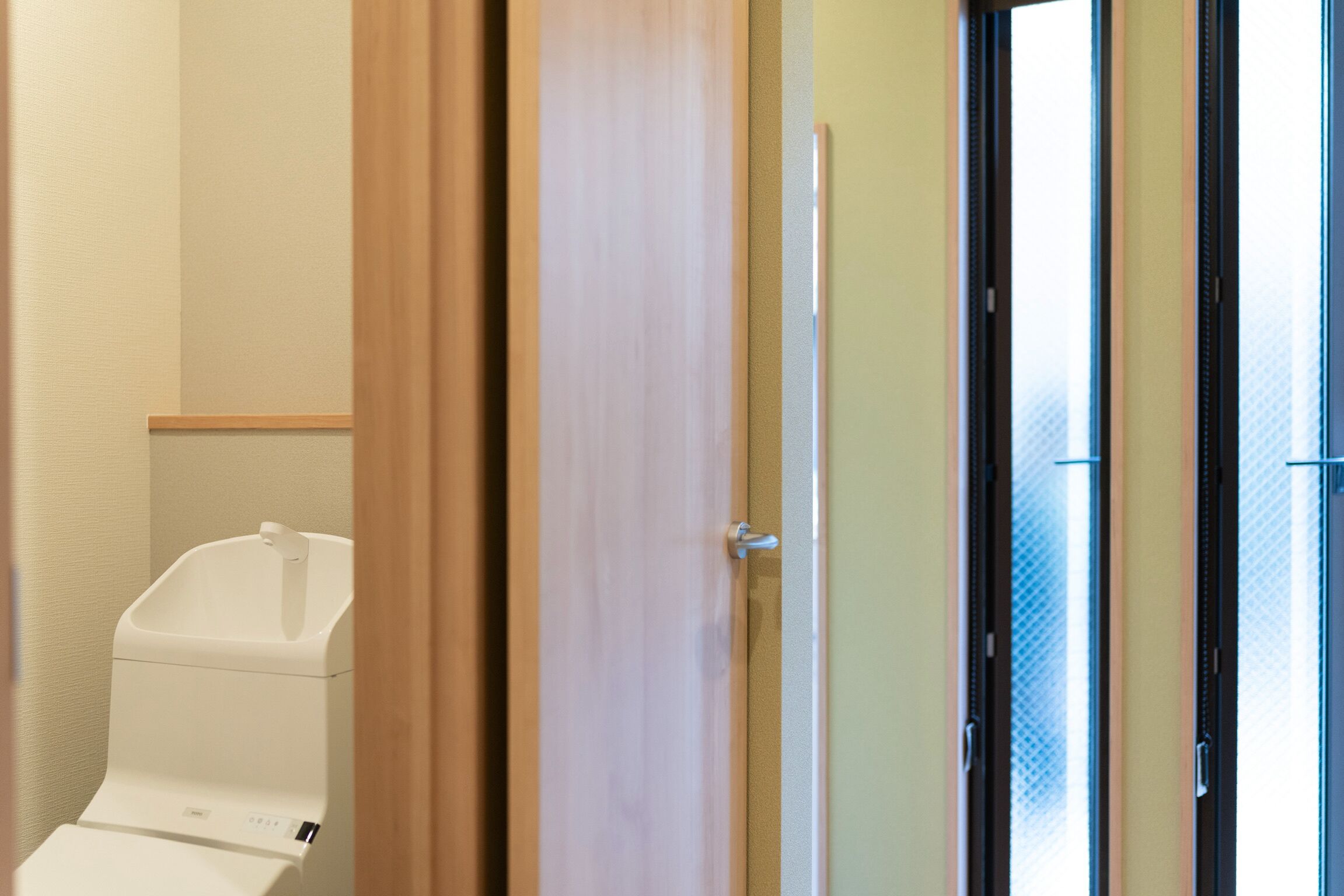 Une salle de bain avec des toilettes, une porte en bois et une porte en verre donnant sur l’extérieur.