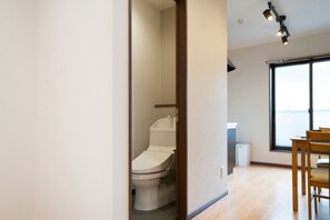Un intérieur moderne avec des toilettes apparentes, un coin repas avec des chaises et une grande fenêtre laissant entrer la lumière naturelle.