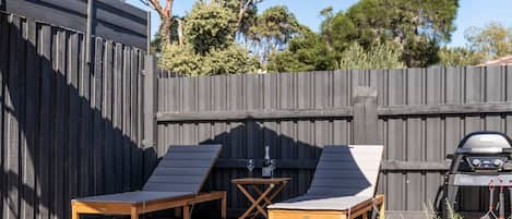 A wooden deck with two lounge chairs and a barbecue grill.