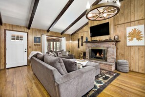 Ein gemütliches Wohnzimmer mit einer Eckcouch, einem Kamin, Holzwänden und einem Deckenventilator.