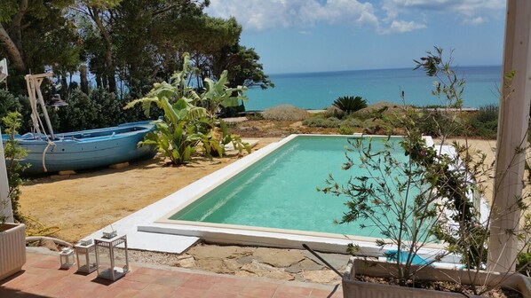 A swimming pool with a view of the sea, surrounded by greenery and a few boats.
