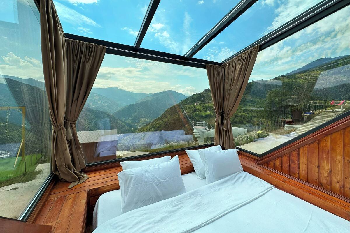 Quarto com uma janela grande, piso de madeira e roupa de cama branca.