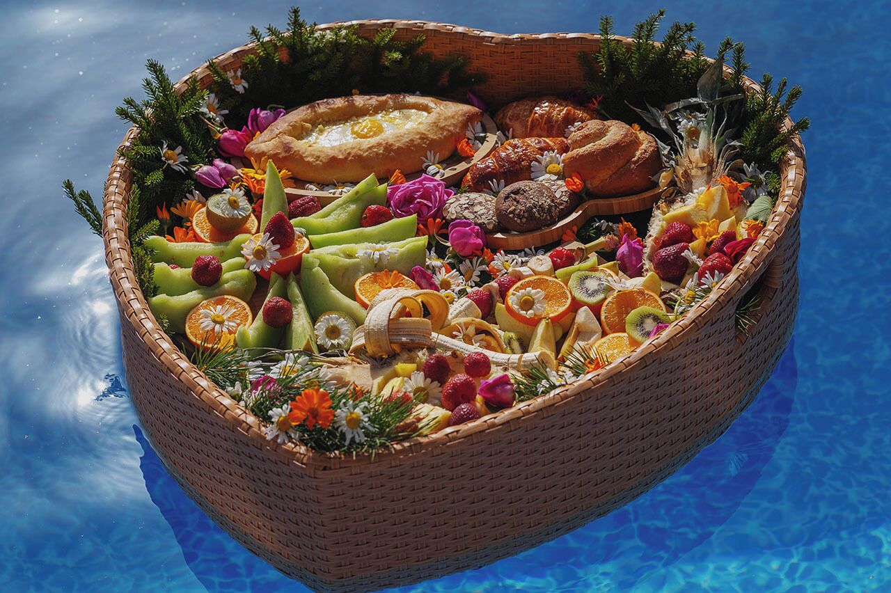 Un panier en osier rempli de fruits, de fleurs et de pâtisseries, flottant sur une piscine.