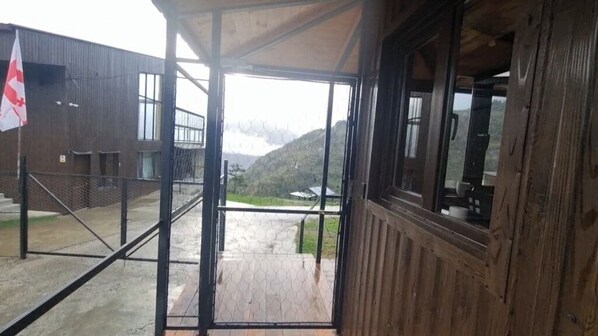 A wooden building with a covered entrance and a view of a hilly landscape. - NIka Hotel and Club (Chanchkhalo)