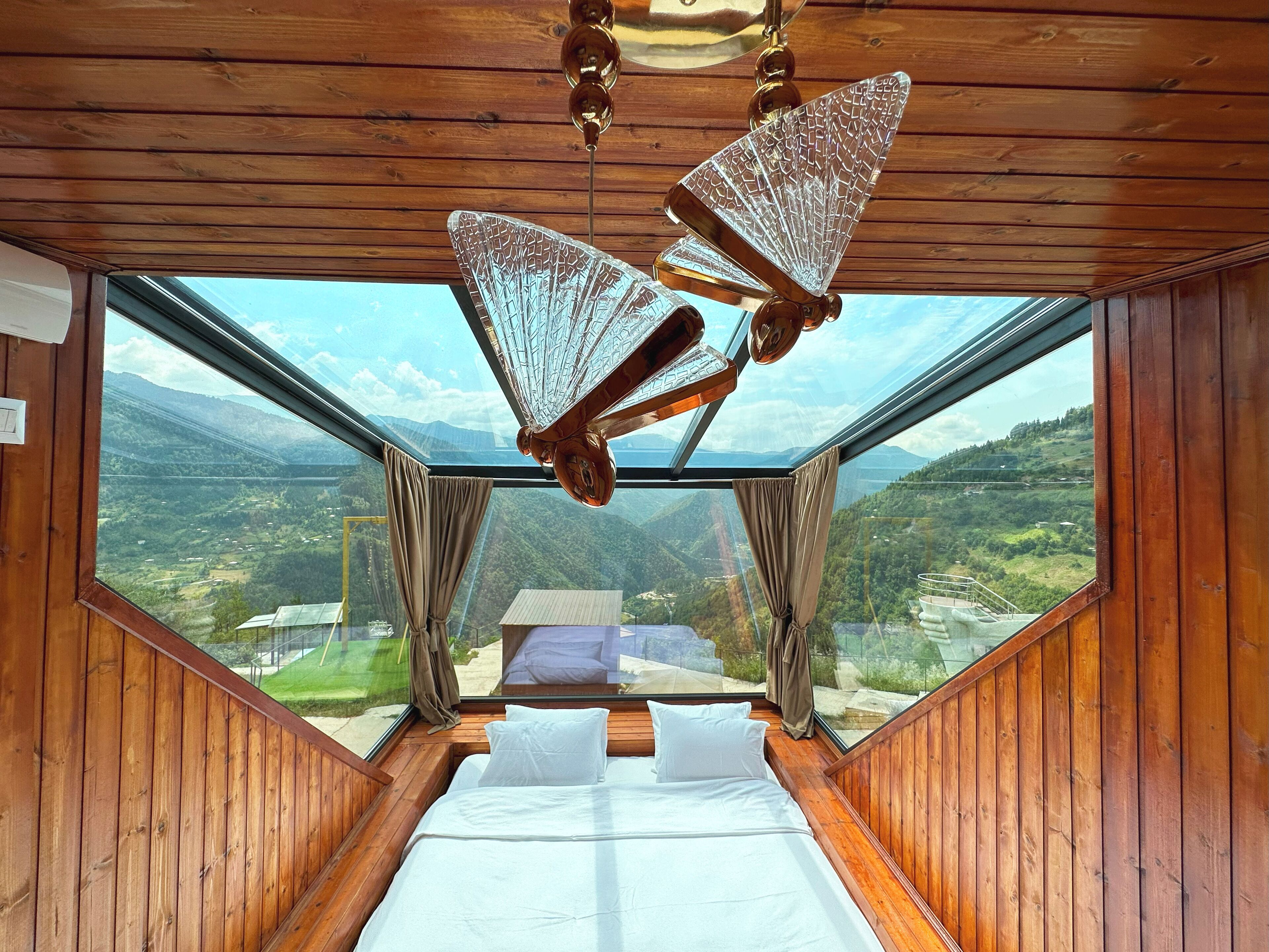 A bedroom with a large bed, wooden walls, and a view of a valley.