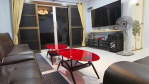 Una sala de estar con un sofá, dos mesas de vidrio rojas, un ventilador y un ventanal corredero.