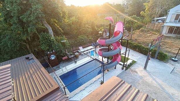 Un patio trasero con piscina, un tobogán de varios niveles y una terraza de madera.