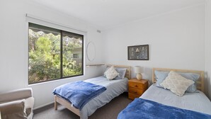 A bedroom with two single beds, a wooden nightstand, a chair, and a large window with a view of greenery.