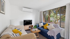 A living room with a television, two sofas, a coffee table, and a large window with a view of trees.