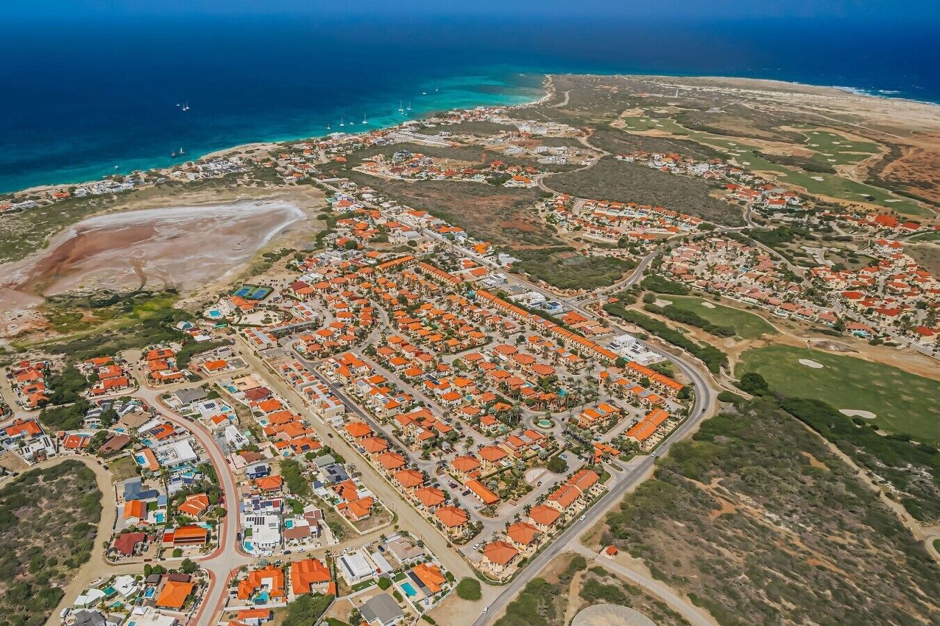 An aerial view of a coastal residential area with houses, roads, and a beach.