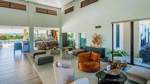 Amplia sala de estar con múltiples opciones de asientos, una zona de bar y ventanas grandes que ofrecen vistas al exterior.