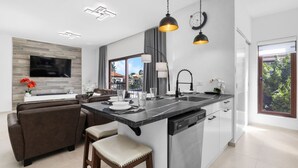 Una cocina moderna con una isla central, un área de comedor con sofá y un televisor montado en la pared.