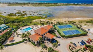 Vista aérea de un complejo turístico con piscina, canchas de tenis y acceso a la playa.