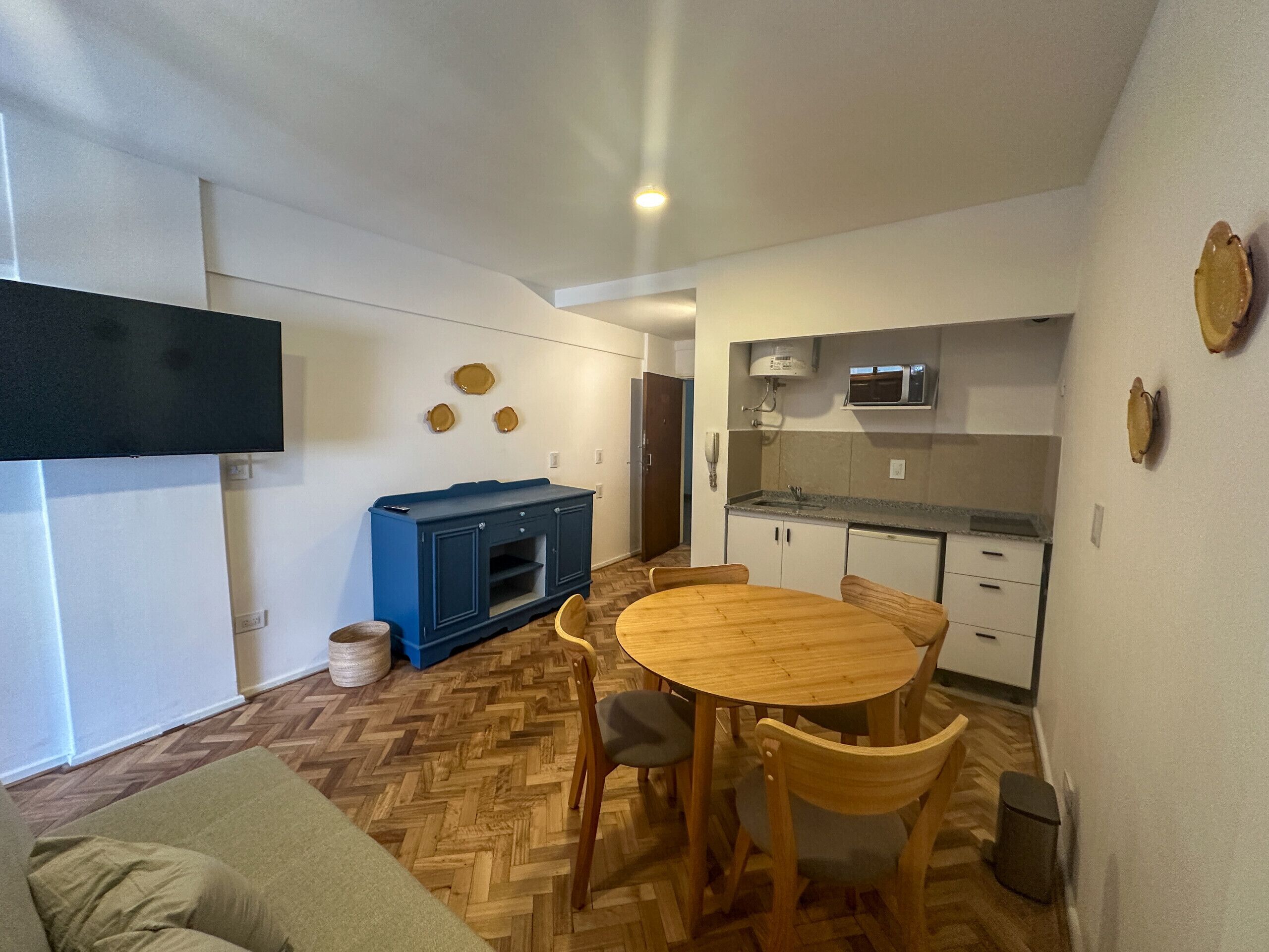 A compact living space with a dining area, kitchenette, and a television mounted on the wall.
