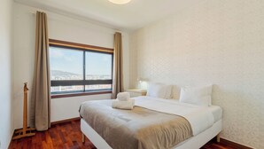Ein Hotelzimmer mit einem großen Bett, Holzboden, einem Fenster mit Stadtblick und einer Wand mit Muster.