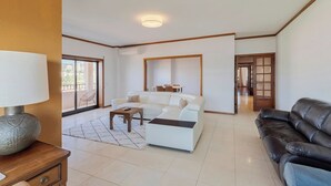 Ein geräumiges Wohnzimmer mit einem weißen Sofa, einem schwarzen Ledersessel und einem Holztisch.
