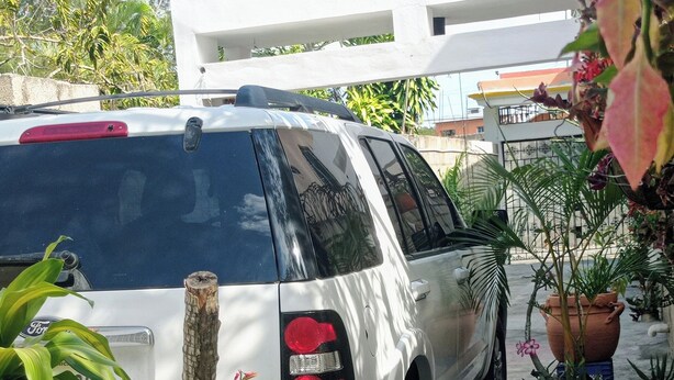 Ein weißer SUV steht auf einer Auffahrt mit Blumentöpfen und einem kleinen Tisch mit einer Tasse darauf.
