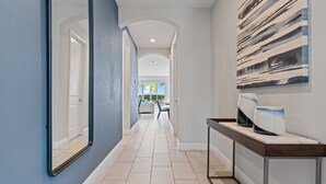 A hallway with a blue wall, a mirror, a tiled floor, and a view into a dining area.