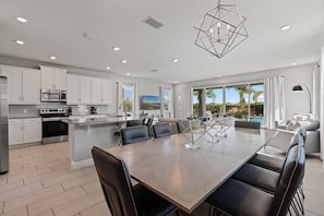 A modern kitchen with white cabinets, stainless steel appliances, and a large island with seating. - 6BR house with pool table near Disney area (Kissimmee)