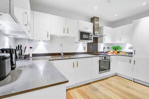 A modern kitchen with white cabinetry, stainless steel appliances, and a wooden floor.