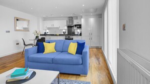 Una sala de estar moderna con un sofá azul, un comedor y una cocina al fondo.