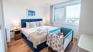 Un dormitorio con cama, mesita de noche, ventana con persianas y vista a la ciudad, además de una cuna.