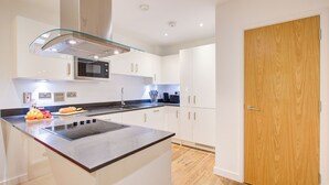 A modern kitchen with a central island, white cabinetry, a microwave, and a wooden door.