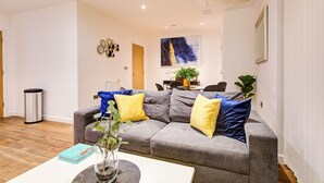 A living room with a grey sofa, yellow and blue cushions, a white coffee table, and a painting on the wall.