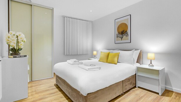 A modern bedroom with a large bed, bedside tables, a wardrobe, and a window with blinds.