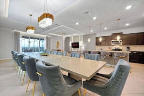 Un comedor moderno con una mesa larga y sillas a juego, una cocina con armarios oscuros y electrodomésticos de acero inoxidable, y un amplio ventanal con vistas.