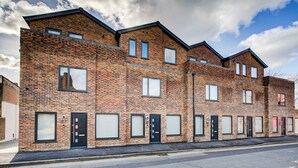 A row of brick townhouses with multiple windows and doors, a flat roof, and a clear sky.