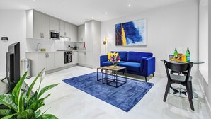 A modern living room with a blue sofa, a coffee table, and a kitchen in the background.