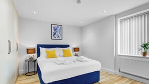 A modern hotel room with a large bed, two bedside tables, a window with blinds, and a wall-mounted artwork.