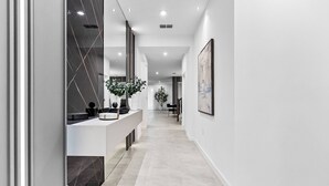 A modern hallway with a white tiled floor, a black and white tiled wall, and a plant on a white console table.