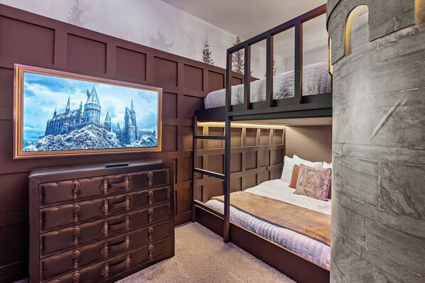 A bunk bed room with a castle-themed wall, a dresser, and a flat-screen TV.
