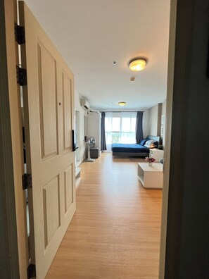 Ein modernes Hotelzimmer mit Holzboden, einem Bett mit blauer Kopfteil, einem weißen Nachttisch und einem großen Fenster mit Vorhängen.