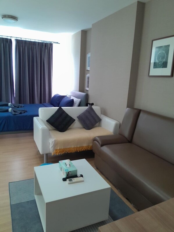 A modern living room with a white sofa, a brown sofa, and a white coffee table. There is a window with curtains, a framed picture on the wall, and a small table with a tissue box and remote control.