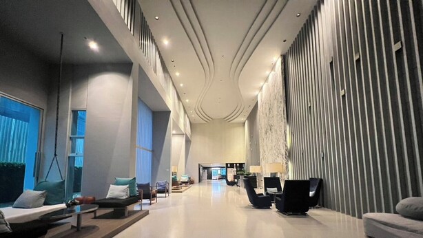 A spacious lobby with a modern design, featuring a seating area with sofas and chairs, a marble column, and a large window providing natural light. - Baan Kiang Fah Hua Hin By Thita (Hua Hin)