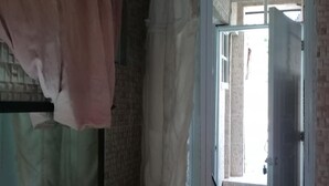Una habitación con pared de ladrillo, una puerta que da a otra estancia, y una lámpara sobre una mesa.