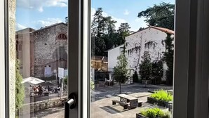 A view through a window of a courtyard with a stone building, a white building, and greenery. - Duplex in charming neighborhood overlooking chateau, close to downtown and all amenities (Clisson)