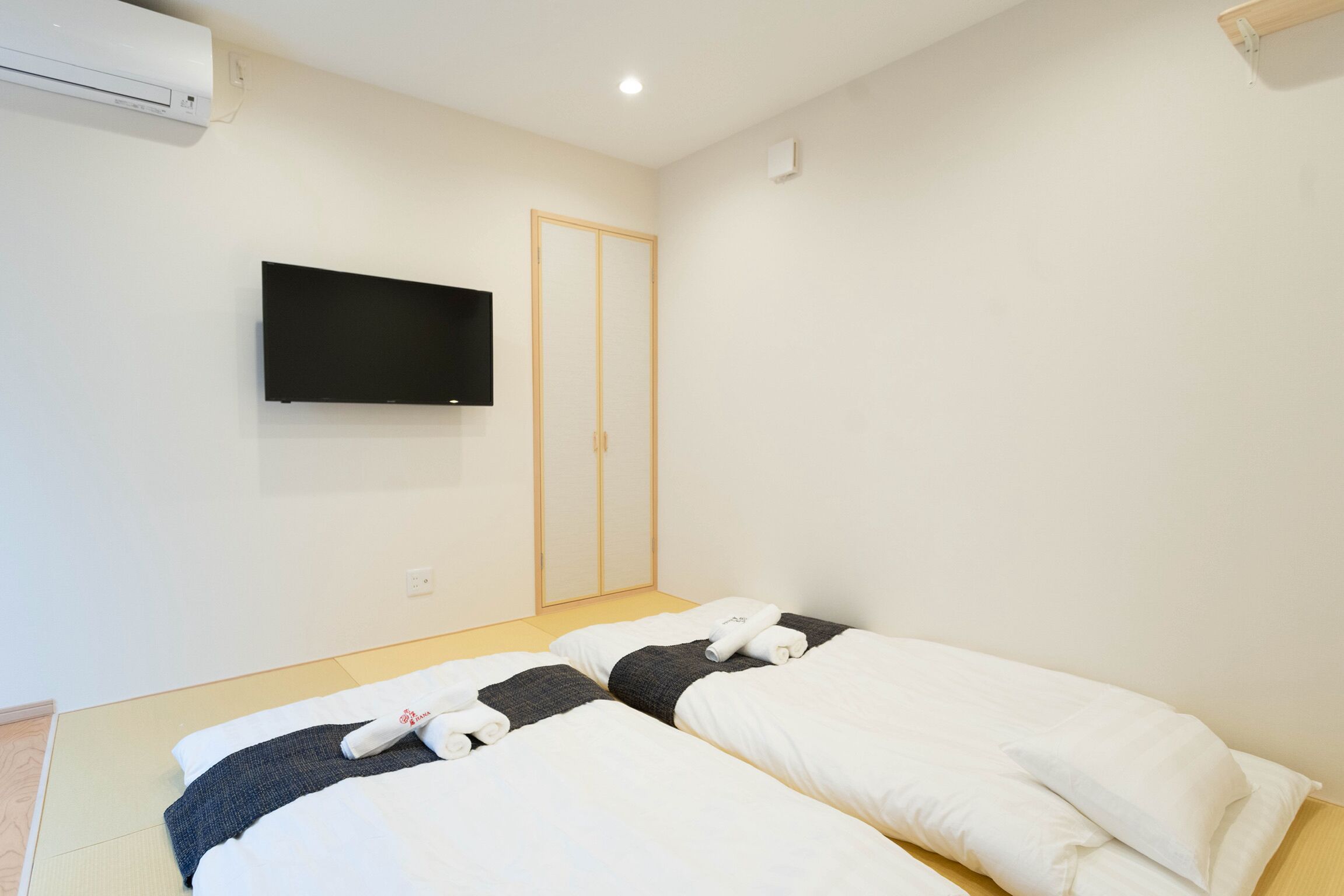 A hotel room with two beds, a flat-screen TV mounted on the wall, and a wooden wardrobe.