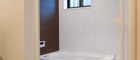 A bathroom with a bathtub, a window, and a wooden wall.
